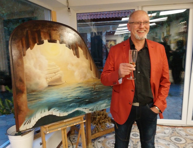 Pan Jiří Polešák se sklenkou vína vedle svého obrazu